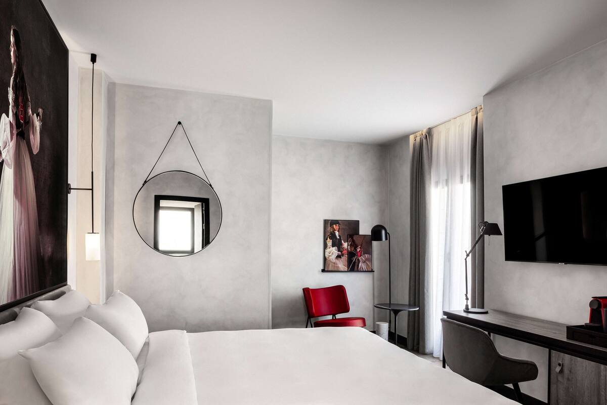 Een moderne hotelkamer met een groot bed, een bureau, een televisie en een rode stoel.