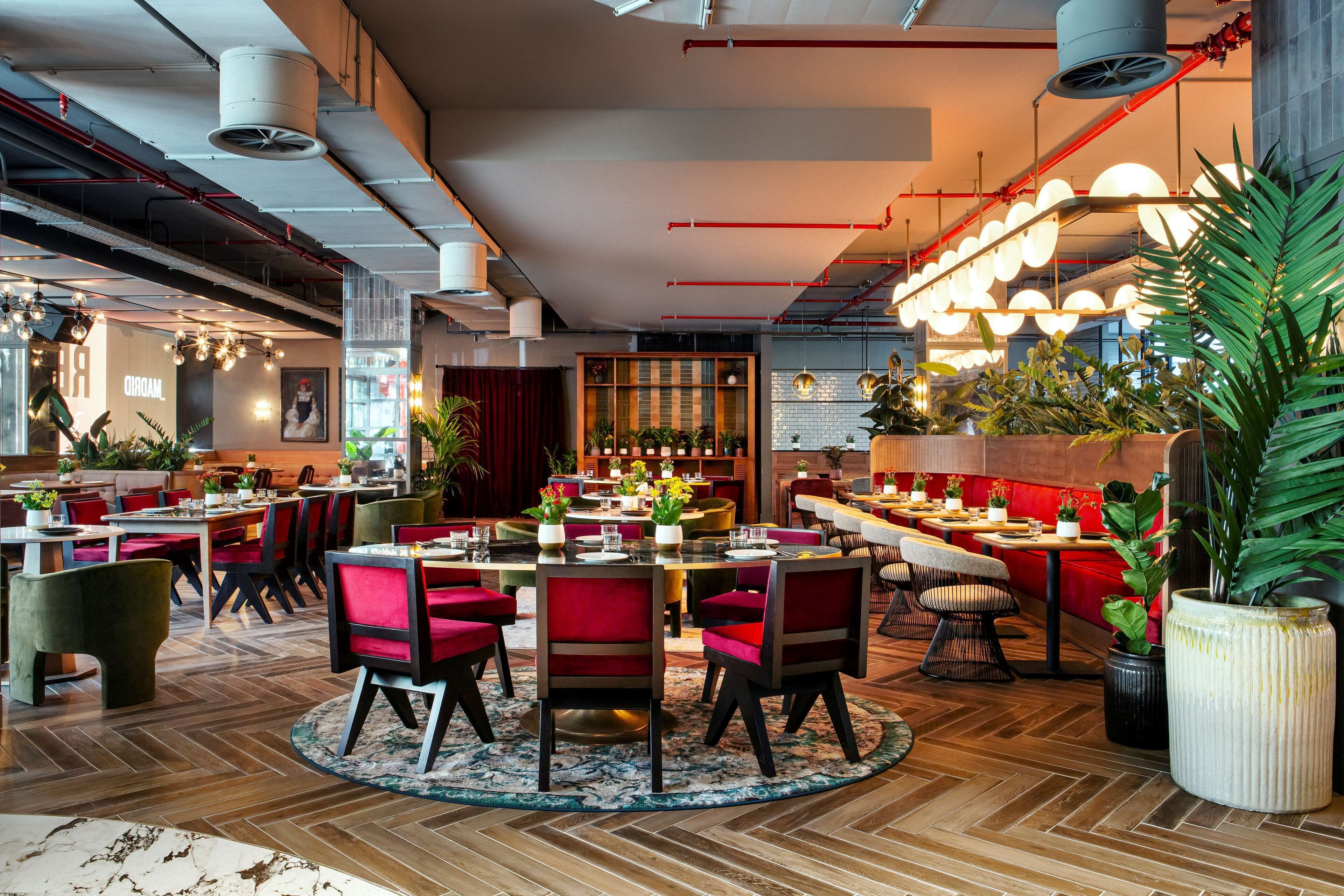 Un restaurant moderne avec des tables rondes, des chaises rouges et des plantes en pot.
