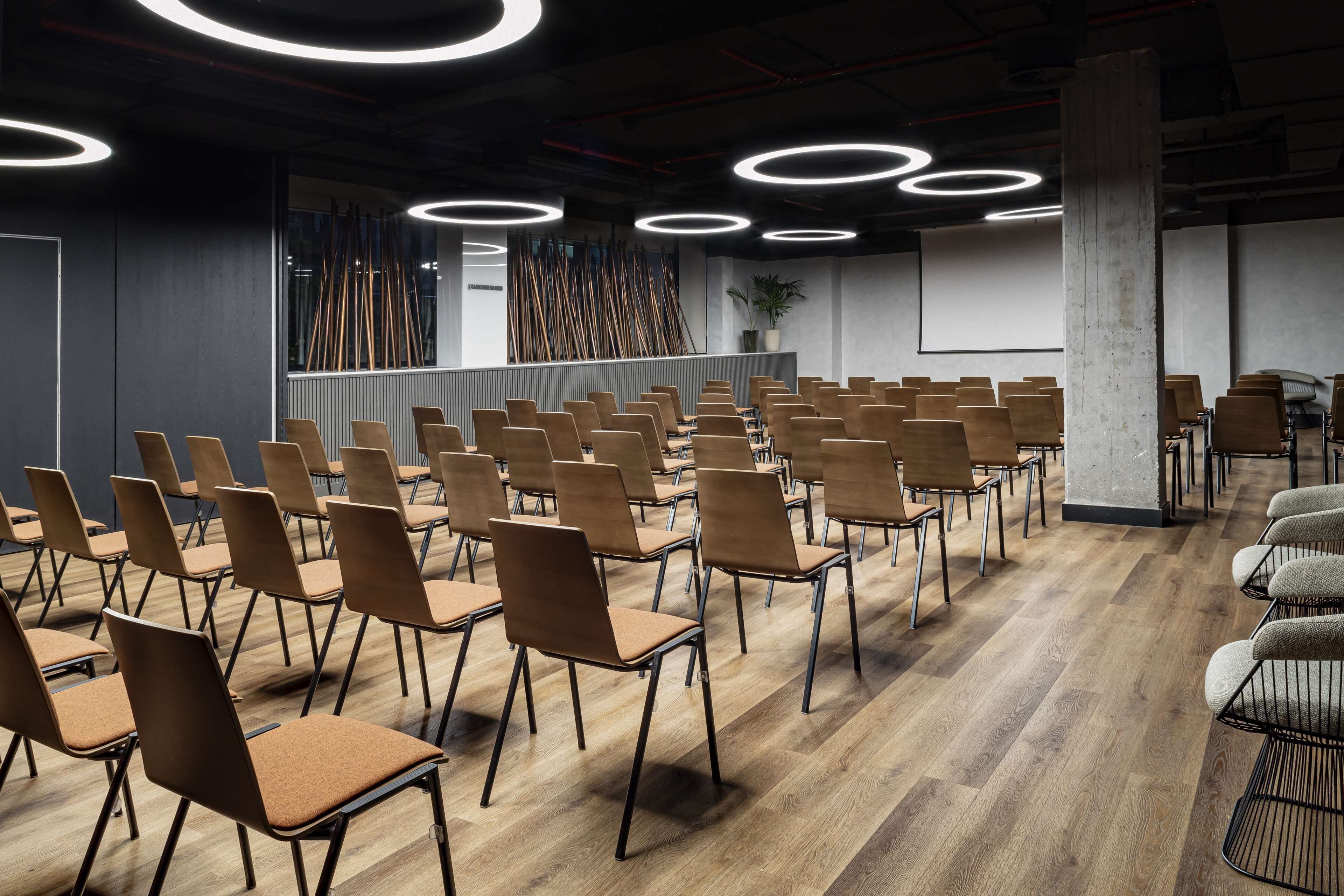 Ein Konferenzraum mit Reihen von Stühlen, einer großen Leinwand und moderner Beleuchtung.