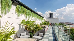 A rooftop terrace with outdoor seating, a checkered floor, and hanging plants.