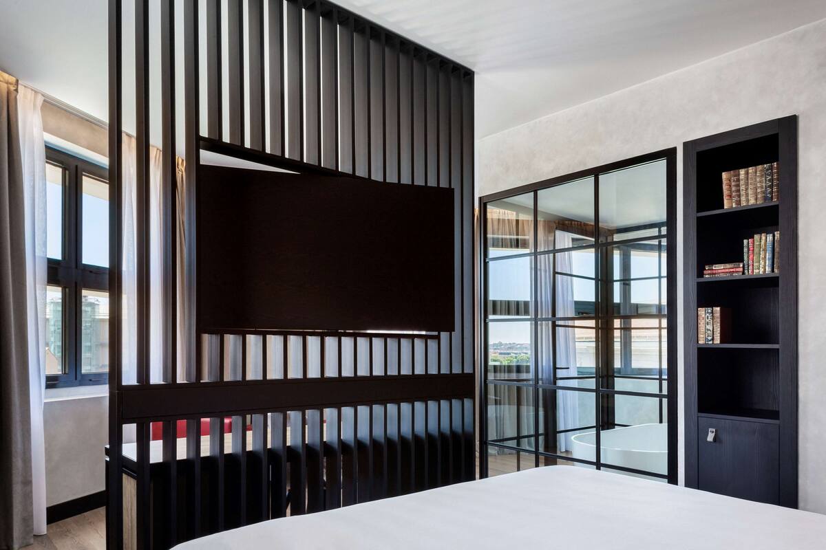 Een moderne slaapkamer met een groot bed, een schuifdeur naar een balkon en een donkere boekenkast.
