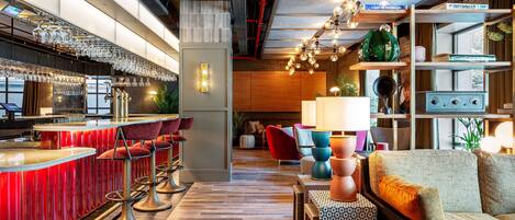 A modern bar area with red bar stools, a wooden floor, and a seating area with a sofa and armchairs.