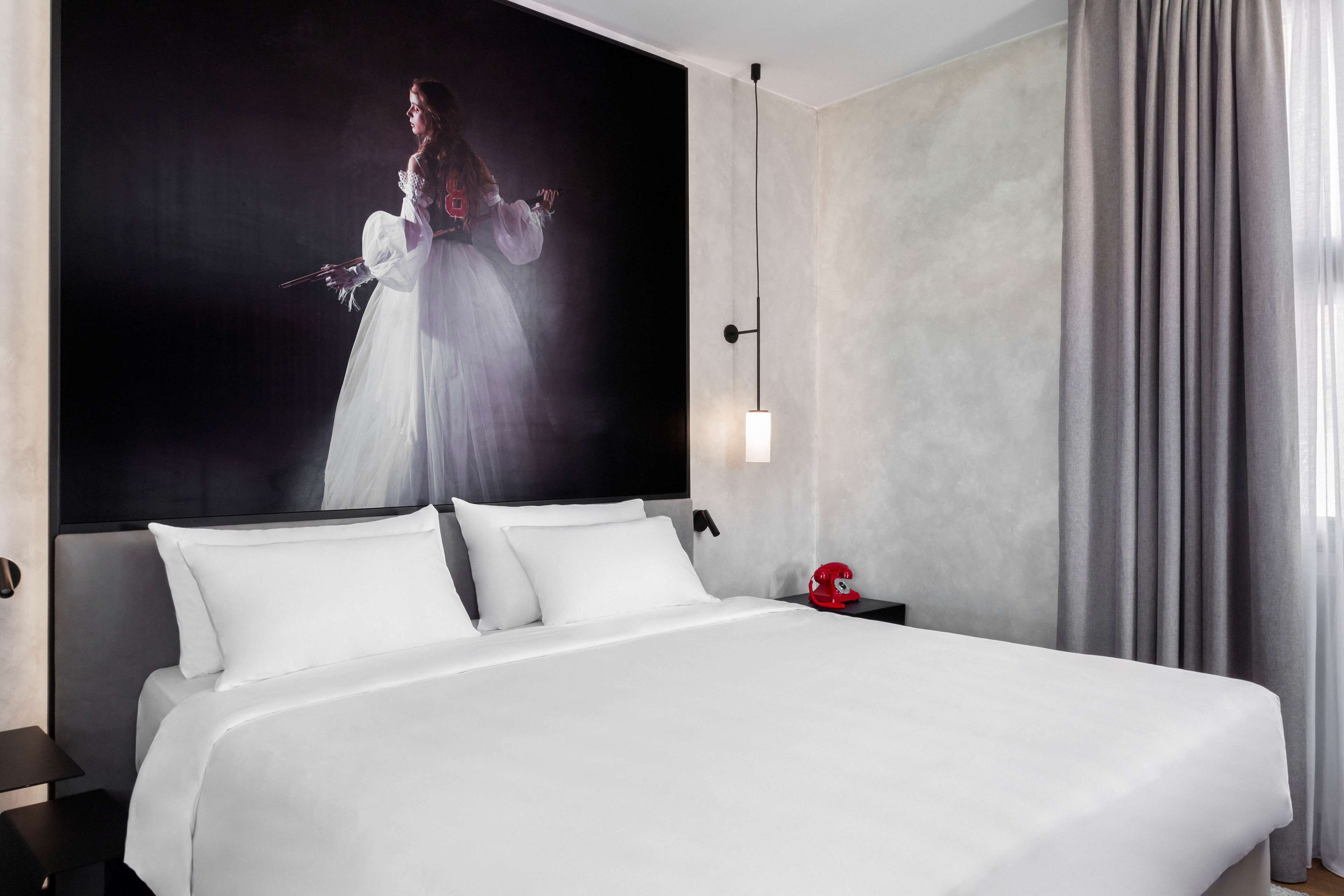 Una habitación de hotel con una cama grande, un cabecero, una mesita de noche y una lámpara fijada a la pared.