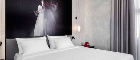 Una habitación de hotel con una cama grande, un cabecero, una mesita de noche y una lámpara fijada a la pared.