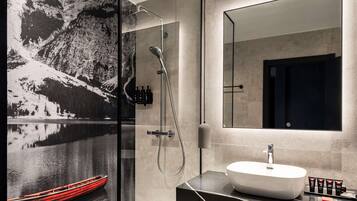 A modern bathroom with a large mirror, a glass-enclosed shower, and a white sink.
