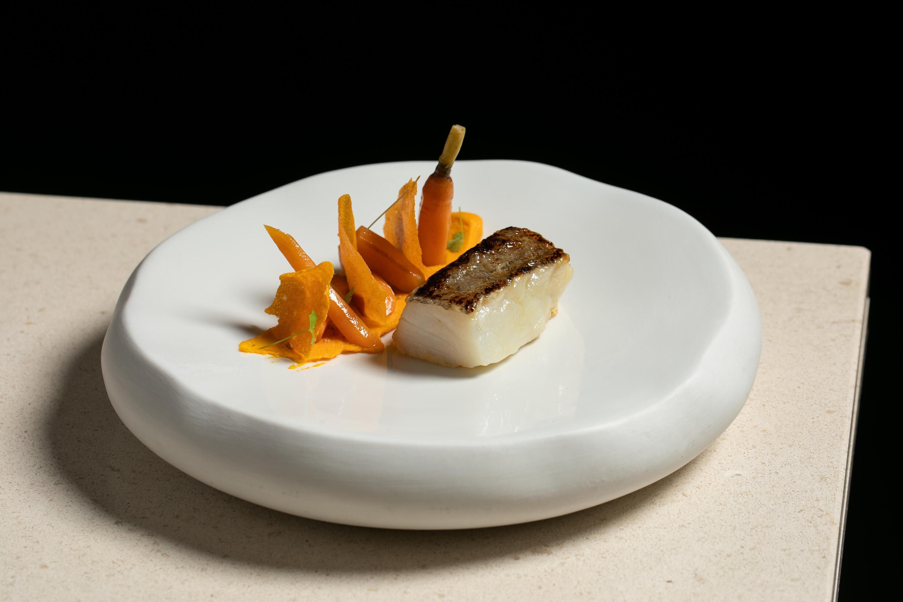Un plato blanco con un trozo de pescado y una guarnición de zanahoria.