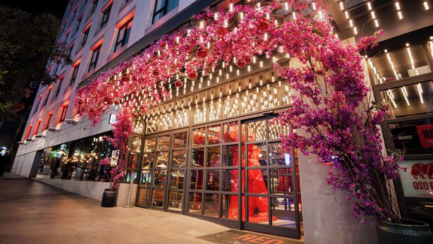A hotel facade with a modern design, large windows, and a decorative arch of pink flowers.