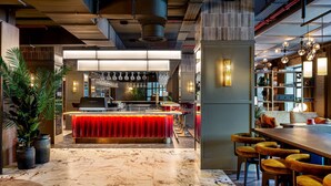 A modern bar area with a red bar counter, marble flooring, and a seating area with yellow chairs.