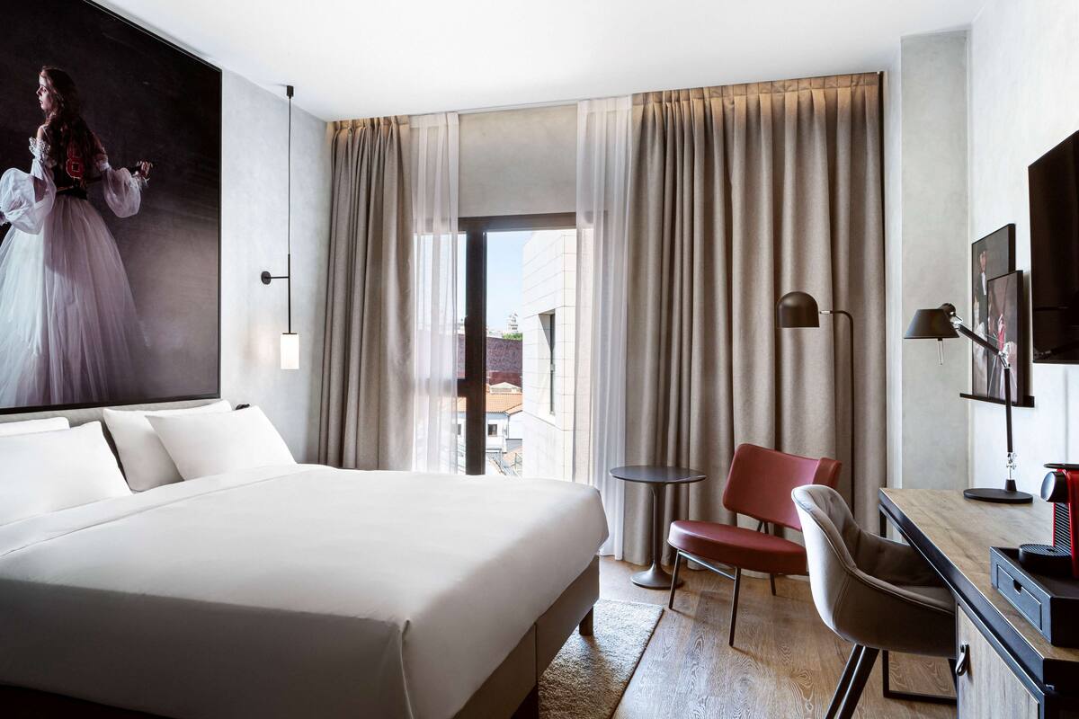 Een hotelkamer met een groot bed, een bureau met stoel, een televisie en een schilderij aan de muur.