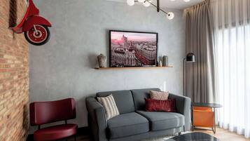 A modern living room with a grey sofa, a red chair, a black coffee table, and a cityscape painting on the wall.