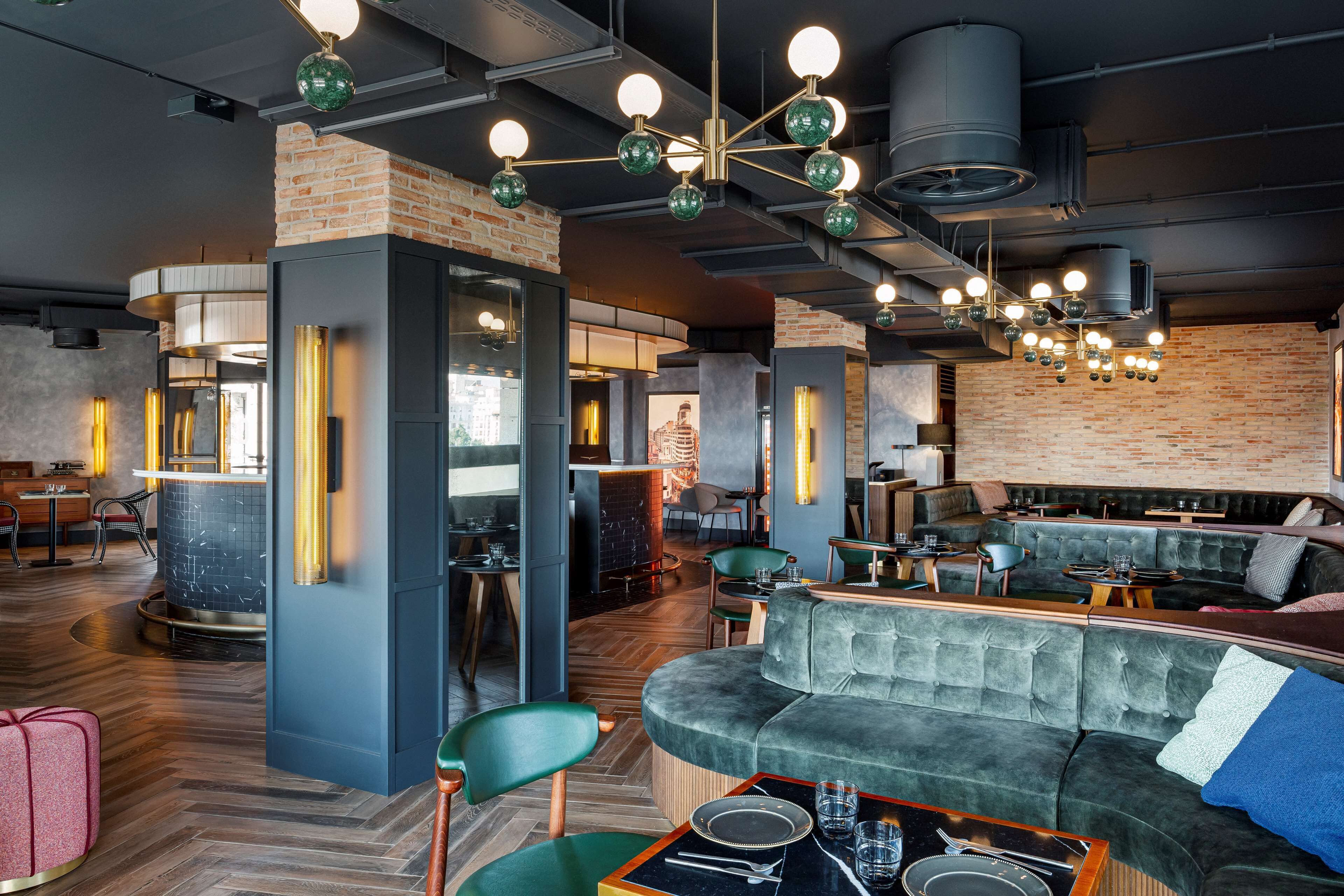 A modern interior with a brick wall, green upholstered seating, and a dining area with a wooden table and chairs.