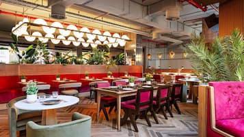 Interior moderno de restaurante con mesas redondas, sillas con cojines rojos y diversas plantas.