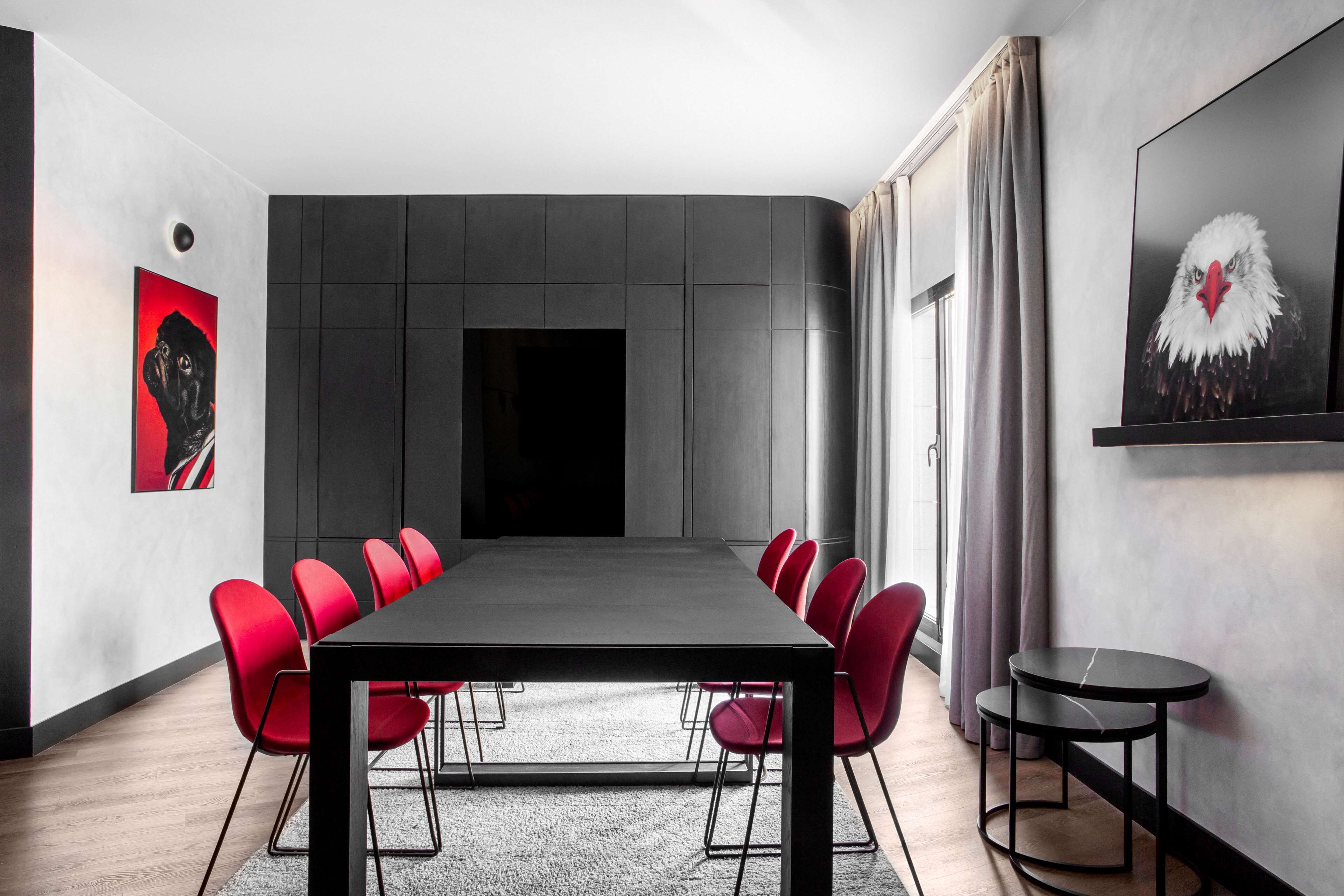 Une salle de conférence moderne, dotée d’une longue table et de chaises rouges, d’une petite table ronde et d’œuvres d’art accrochées aux murs.
