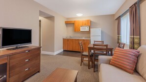A compact living space with a flat-screen TV, wooden furniture, a kitchenette, and a sofa with a striped pillow. - Super 8 by Wyndham Abbotsford BC (Abbotsford)