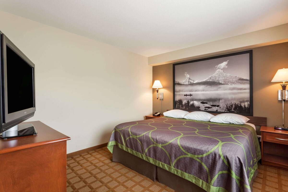 Une chambre d’hôtel avec un lit, un téléviseur à écran plat posé sur une commode en bois, et un grand tableau encadré accroché au mur.