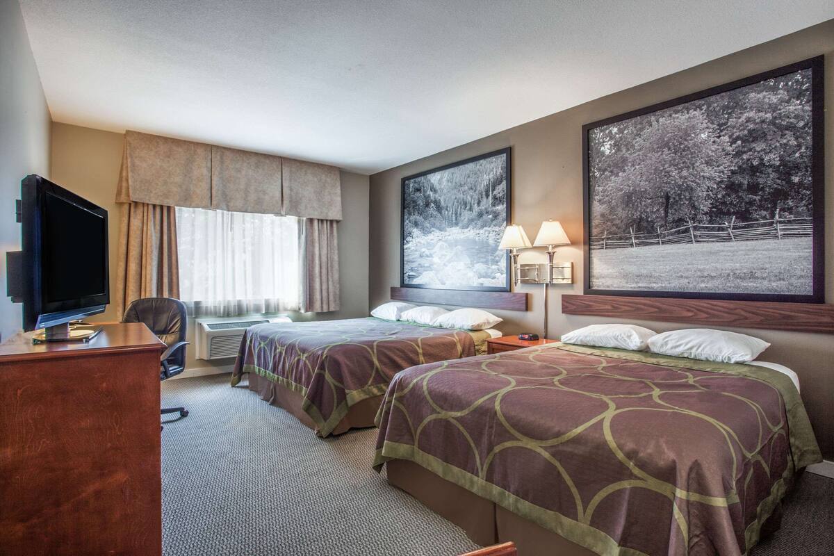 Une chambre d’hôtel avec deux lits, un bureau, une télévision et de grandes fenêtres donnant sur la verdure.