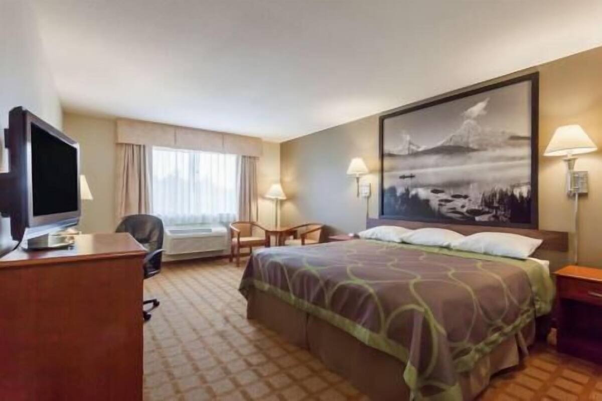Une chambre d’hôtel avec un lit, un bureau avec un ordinateur, une chaise, une fenêtre avec des rideaux et un tableau au mur.
