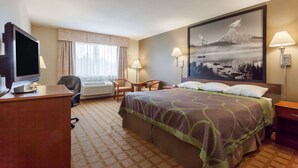 A hotel room with a bed, a desk with a TV, two chairs, a window with curtains, and a large painting on the wall. - Super 8 by Wyndham Abbotsford BC (Abbotsford)