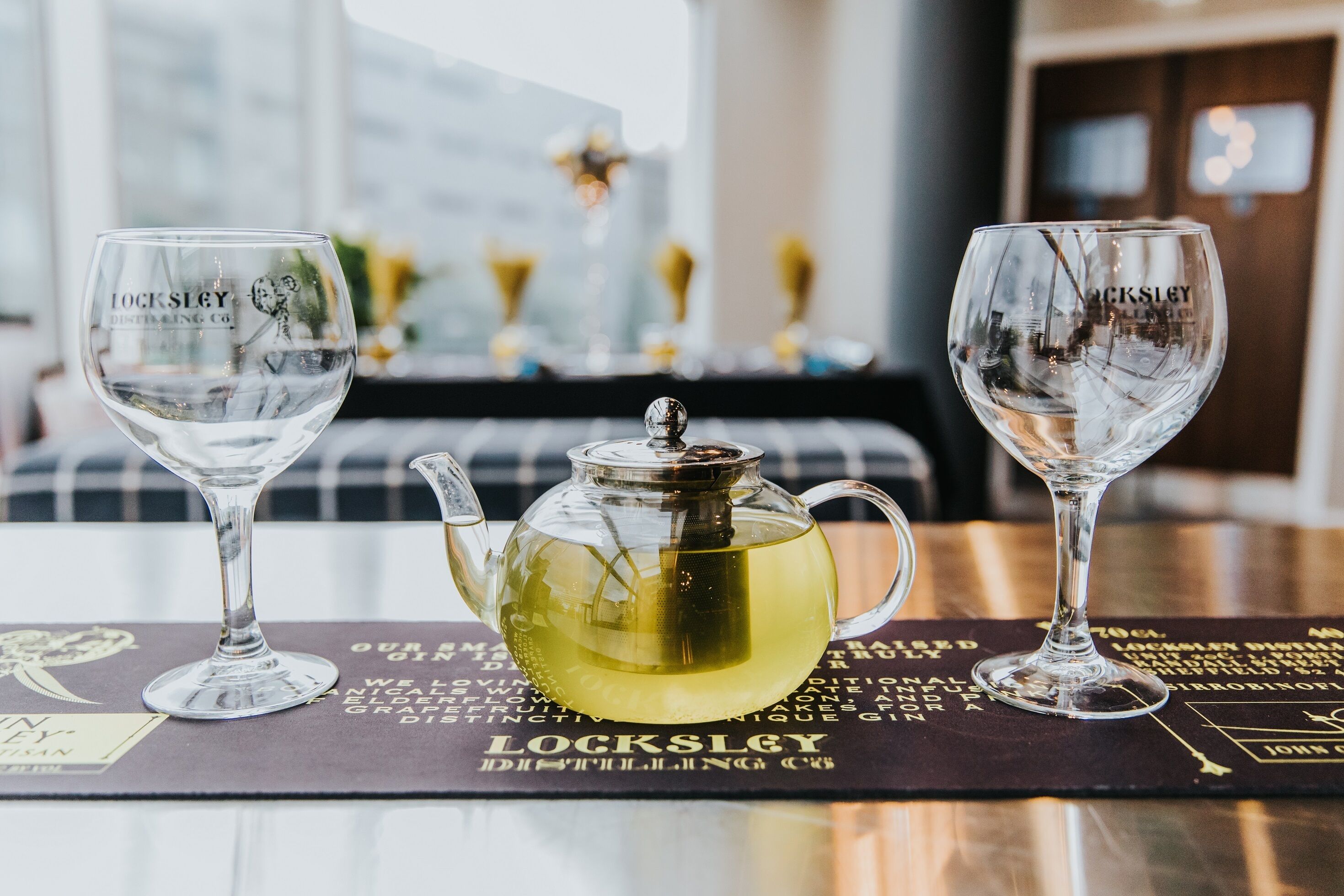 Two clear glasses and a teapot on a table with a placemat displaying text.
