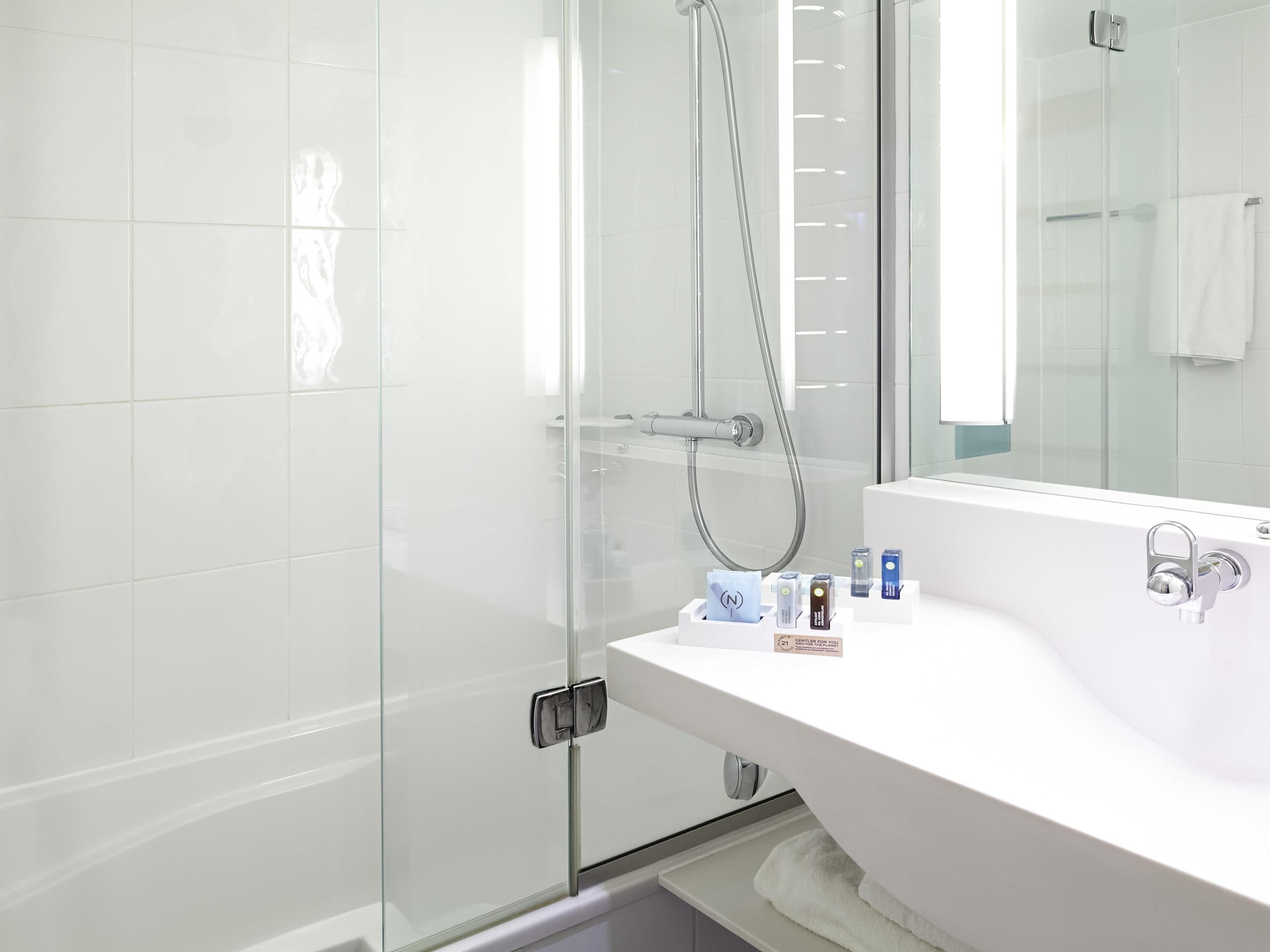 A modern bathroom with a glass shower enclosure, a white sink with toiletries, and a large mirror.