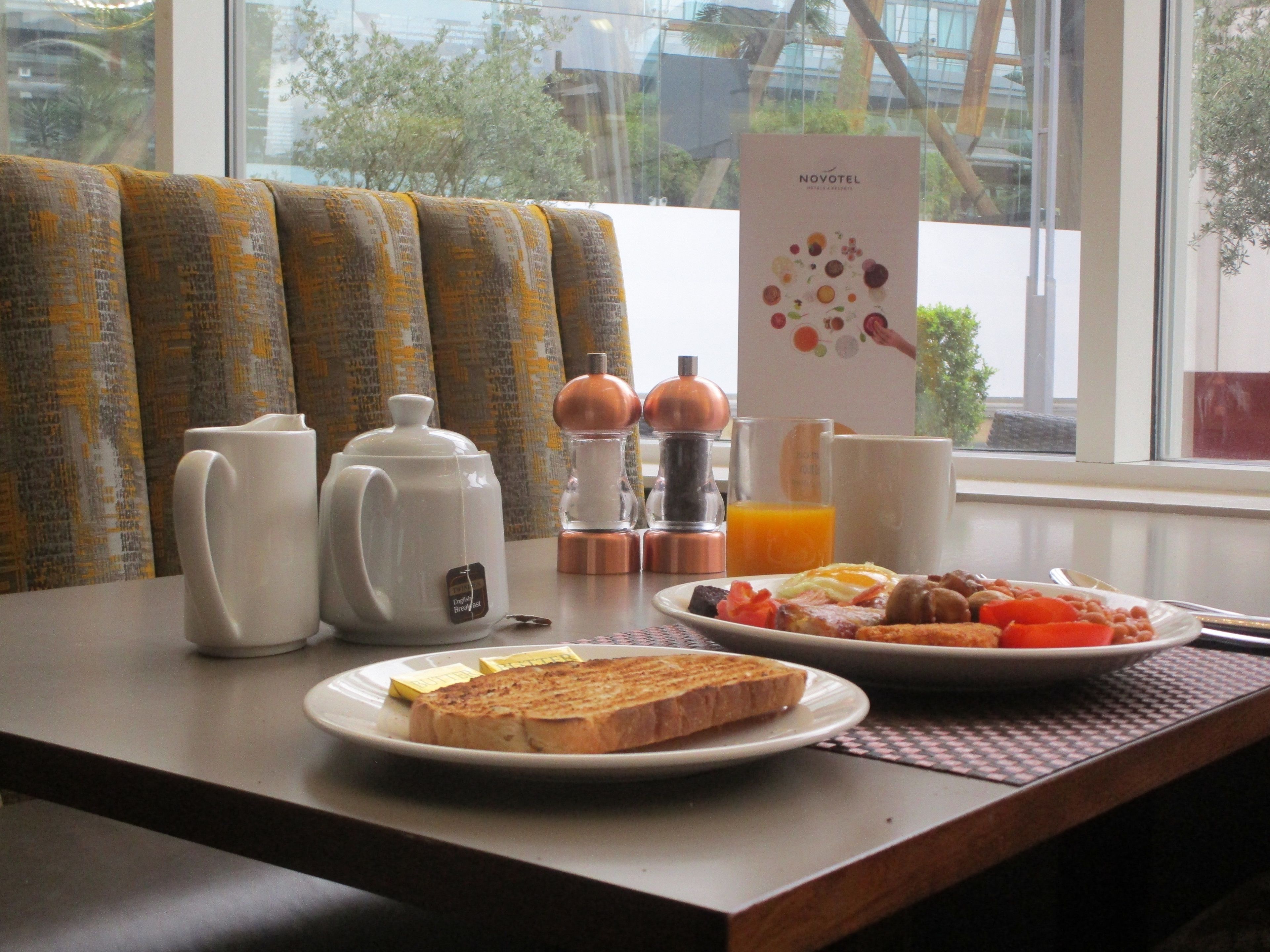 A breakfast setup with toast, eggs, and orange juice on a table, next to a window with a view of trees and buildings.
