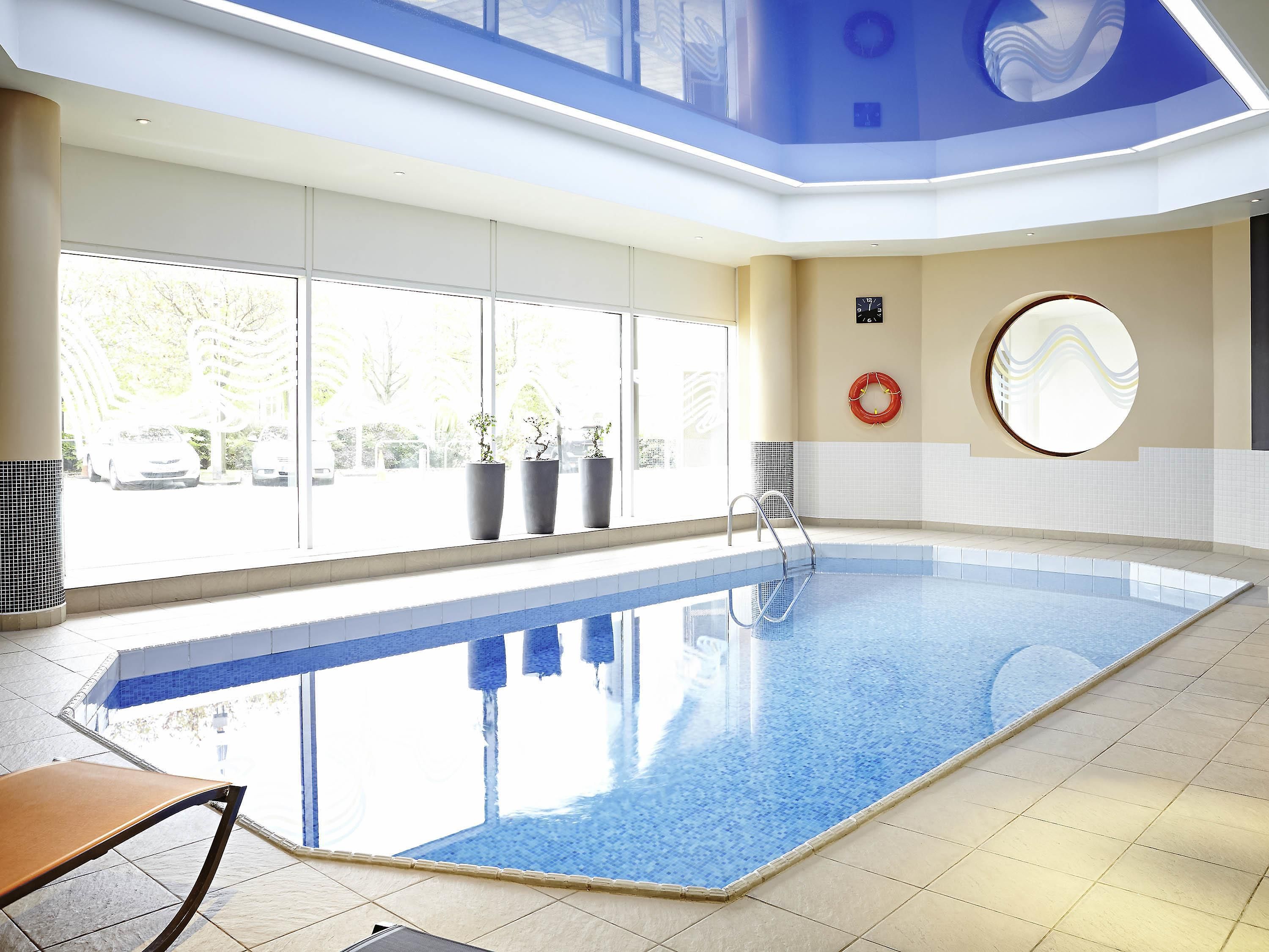 An indoor swimming pool with a clear view of the outside, a lifebuoy on the wall, and a bench by the pool.