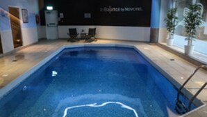 A swimming pool with a tiled deck, a wall with a sign, and two chairs. - Novotel Sheffield Centre (Sheffield)