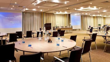 A hotel meeting room with round tables, chairs, a projector screen, and a presentation screen.