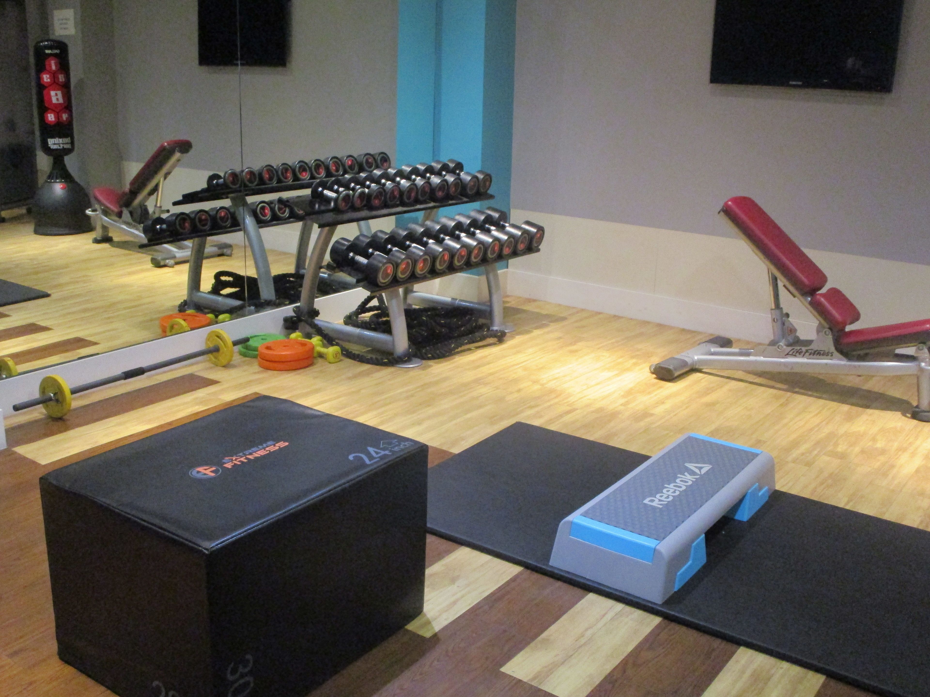 Un gimnasio con equipamiento para levantamiento de pesas, una banca y colchonetas de ejercicio.