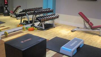 Un gimnasio con equipamiento para levantamiento de pesas, una banca y colchonetas de ejercicio.
