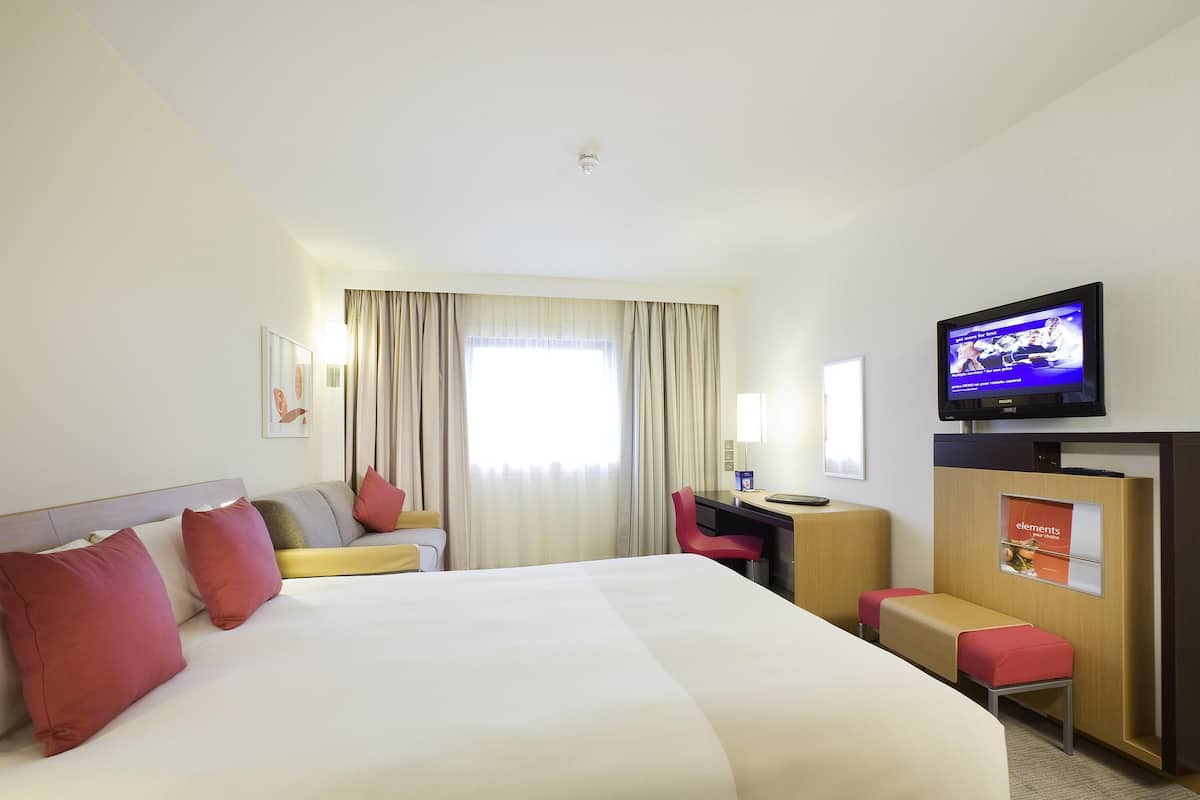 A hotel room with a large bed, a desk, a chair, a television, and a window with curtains.