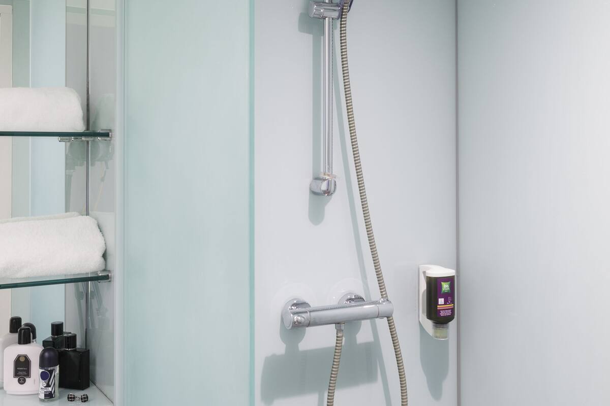 A modern bathroom with a glass shower enclosure, a built-in towel rack, and a control panel.