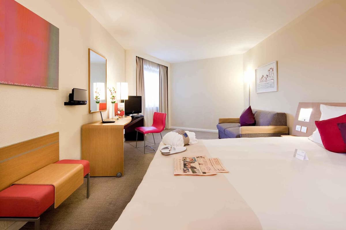 A hotel room with a bed, a desk, a chair, a sofa, and a television.
