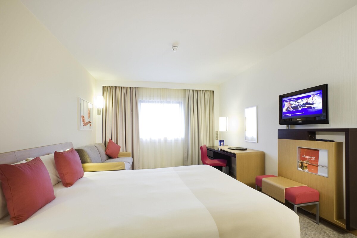 A hotel room with a large bed, a desk, a chair, a television, and a window with curtains.