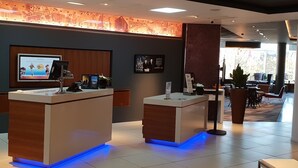 A reception area with two reception desks, a digital screen, framed pictures, and a seating area with tables and chairs. - Novotel Sheffield Centre (Sheffield)