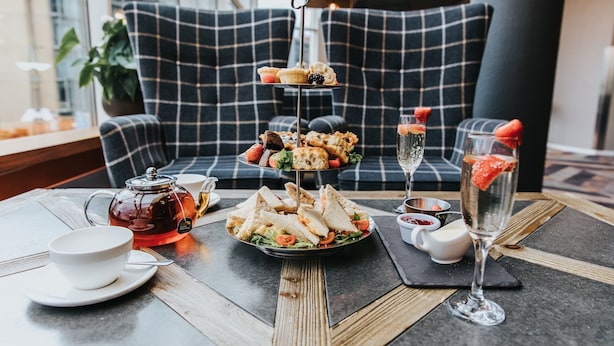 A table set with a tiered dessert stand, a teapot, a cup, and a glass of drink. - Novotel Sheffield Centre (Sheffield)