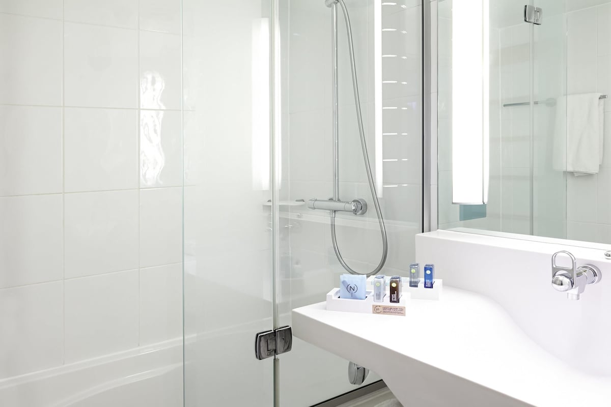 Casa de banho moderna com cabine de duche em vidro, lavatório branco com produtos de higiene e um espelho grande.