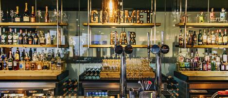 A bar with shelves of liquor bottles, a bar counter with taps, and a sign reading "GOLD BAR".