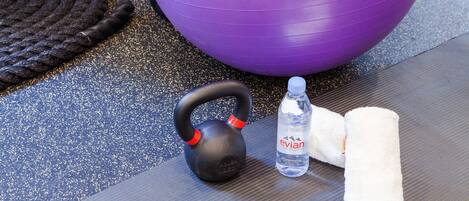 Um kettlebell, uma garrafa de água e uma toalha sobre um tapete texturizado.