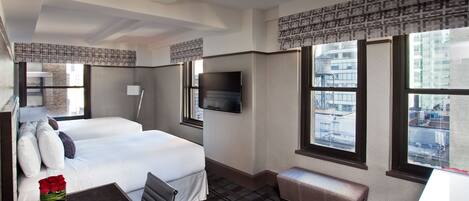 Een hotelkamer met een bed, een bureau, een stoel, een televisie en grote ramen met uitzicht over de stad.