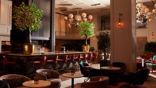 A bar area with a long counter, red chairs, and a large potted plant. There are multiple tables and chairs in the seating area. - Park Central Hotel New York (New York)