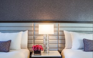 A hotel room with a padded headboard, two beds with white and patterned pillows, a bedside table with a vase of flowers, and a modern lamp. - Park Central Hotel New York (New York)