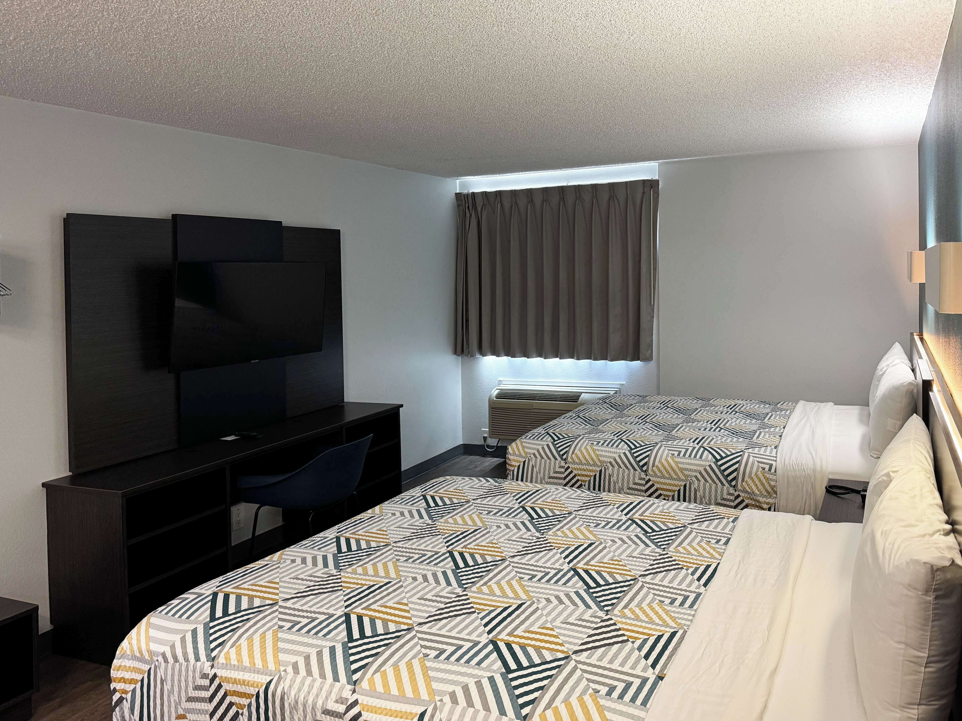 A hotel room with a bed, a desk, a television, and a window with curtains.
