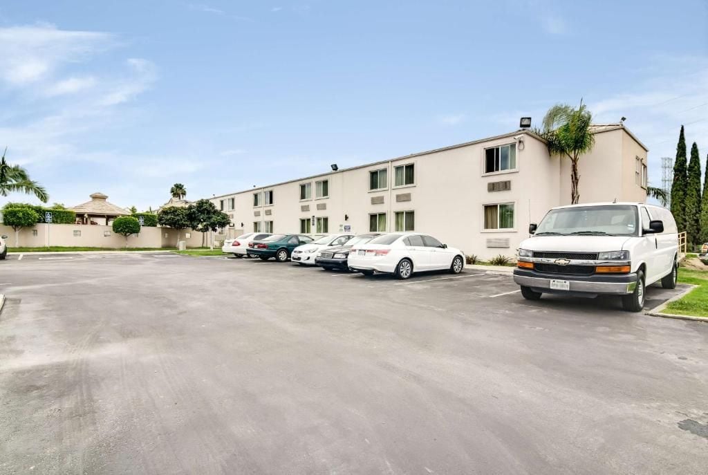 A parking lot with several cars and a white truck parked in front of a building with multiple windows and a flat roof.