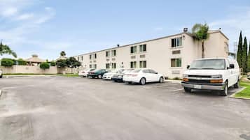 A parking lot with several cars and a white truck parked in front of a building with multiple windows and a flat roof.