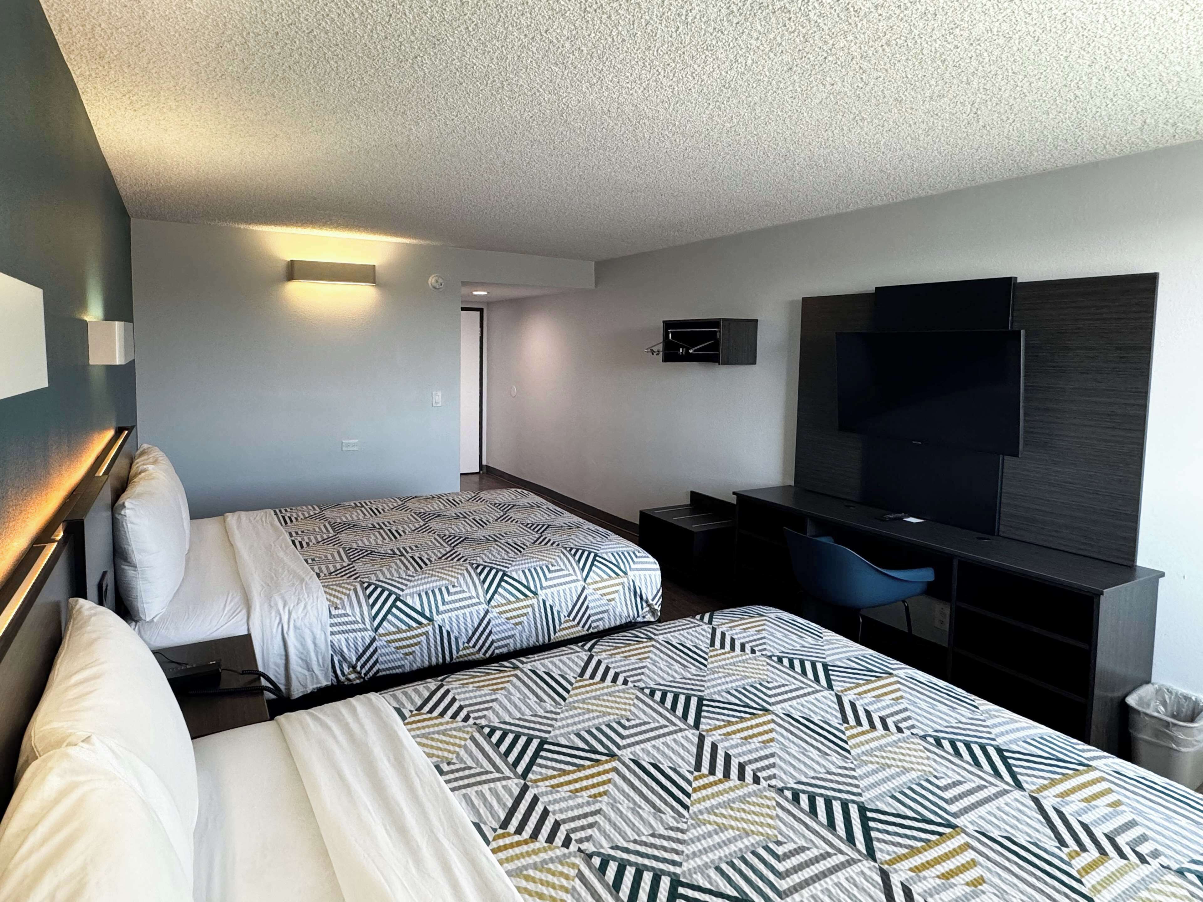 A hotel room with two beds, a desk, a TV, and a trash bin.