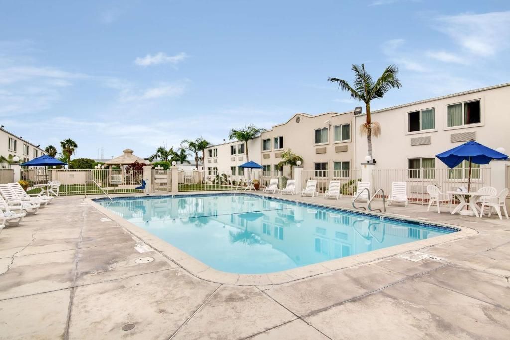 A swimming pool with lounge chairs and umbrellas, surrounded by buildings with balconies.