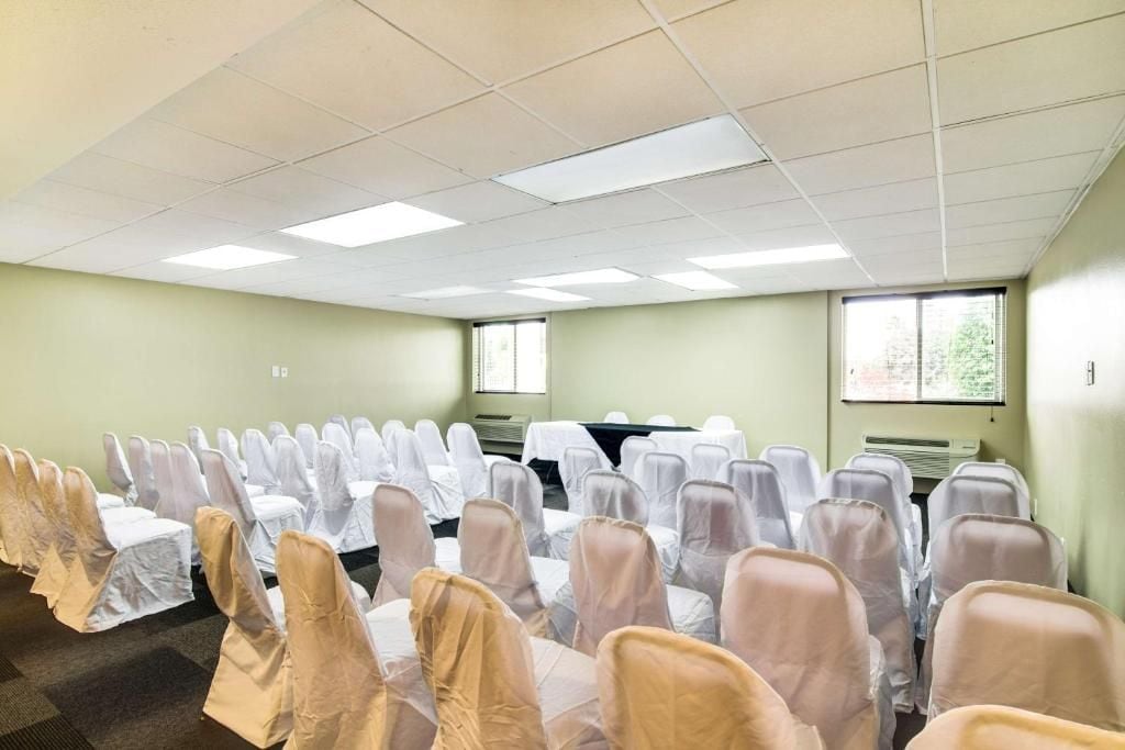 A conference room with rows of chairs covered in white and beige chair covers, a table with a white tablecloth, and a window with blinds.