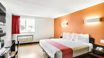 Une chambre d’hôtel comprenant un lit, un bureau, une chaise, une fenêtre avec des rideaux, un radiateur fixé au mur et une table de chevet avec un téléphone.