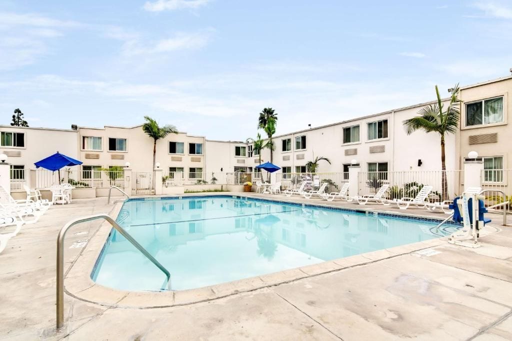 A swimming pool with lounge chairs and umbrellas, surrounded by multi-story buildings with balconies.